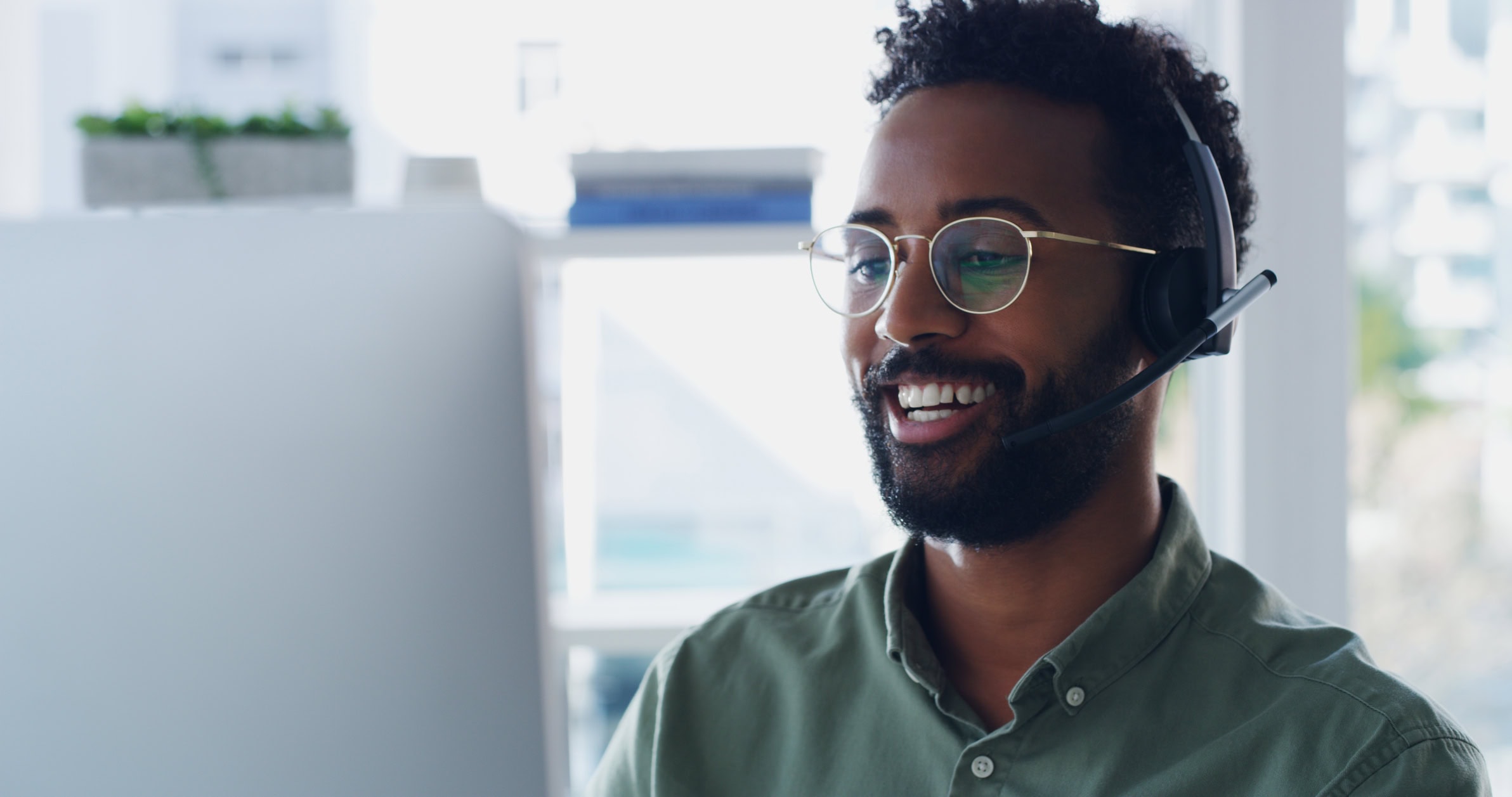 He's always ready to help Shot of a handsome young businessman wearing headsets while working on a computer in his office